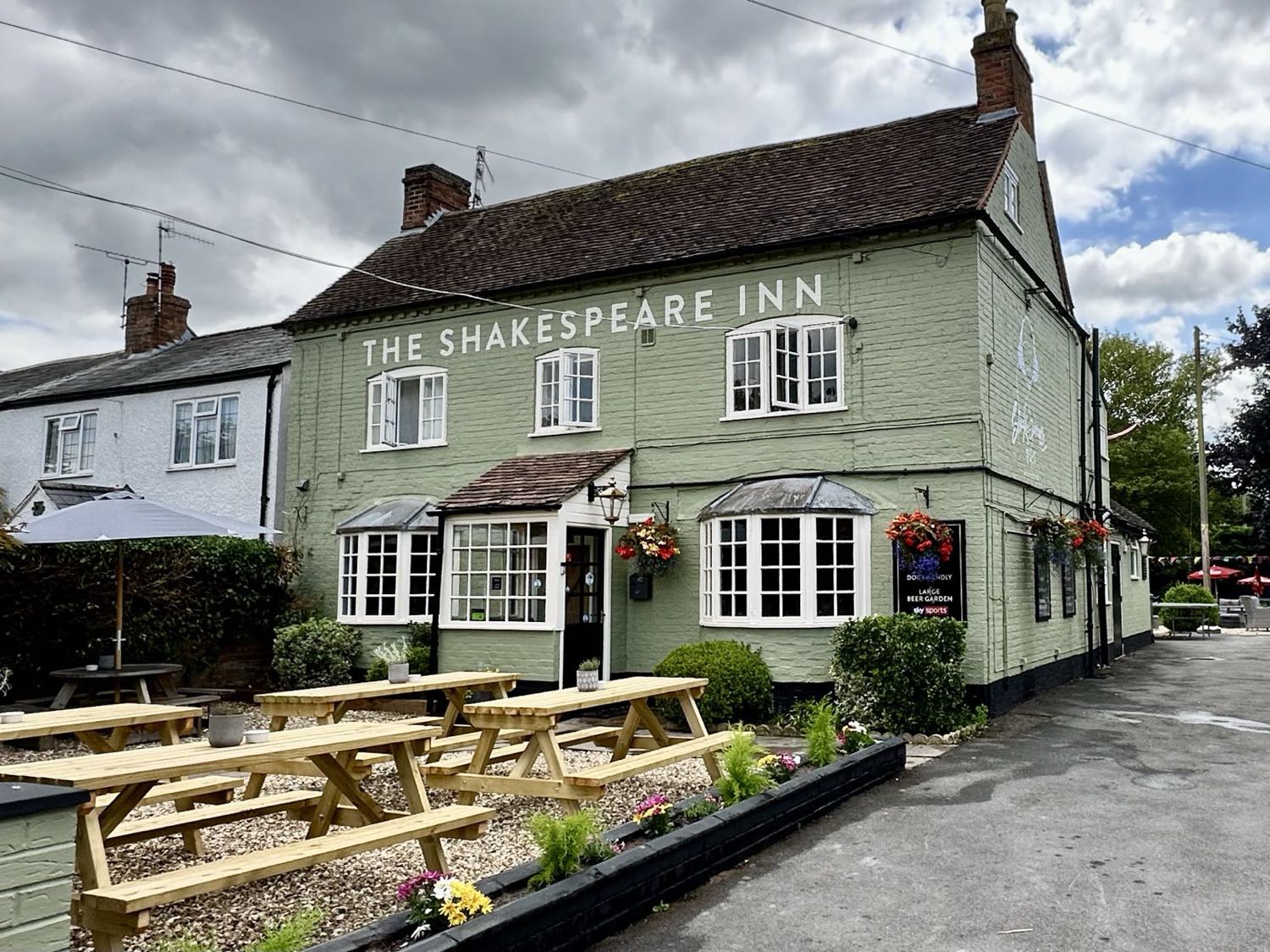 The Shakespeare Inn's sage-green frontage and picnic benches on an overcast day, the pub sign above the door.